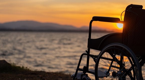 Wheelchair on the sand at a beach with a sunset in the background